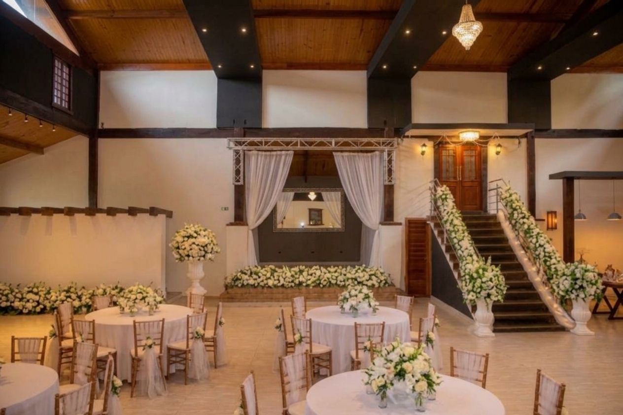 Salão do Castelhano com escada decorada com flores brancas, palco com cortinas e mesas redondas